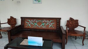 Een houten bank met een bloemenmotief, een glazen tafel met een kaartje en een ingelijst beeld aan de muur.