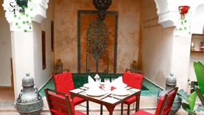 A dining area with a table set for four, surrounded by red chairs, with a decorative wall and a green carpet. - Riad Sassa Finda (Marrakech)