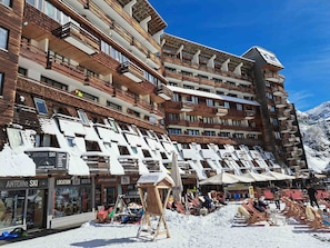 Un hôtel à plusieurs étages doté de balcons, proposant un service de location de matériel de ski et abritant des boutiques au rez-de-chaussée.