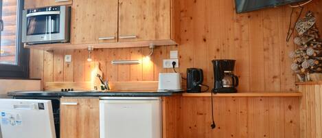 Cocina compacta con armarios de madera, microondas, cafetera y televisor en la pared.
