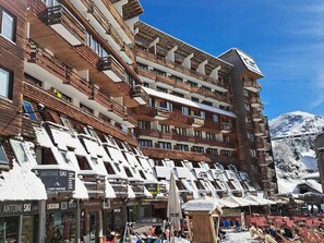 Un hôtel à plusieurs étages doté de balcons, de boutiques de location de matériel de ski et offrant une vue imprenable sur les montagnes.