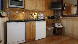 Een kleine keuken met houten kastjes, een magnetron, een koffiezetapparaat en een vaatwasser.