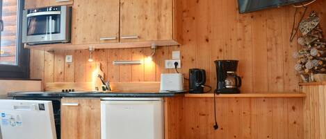 A compact kitchen with wooden cabinets, a microwave, a coffee maker, and a small refrigerator.