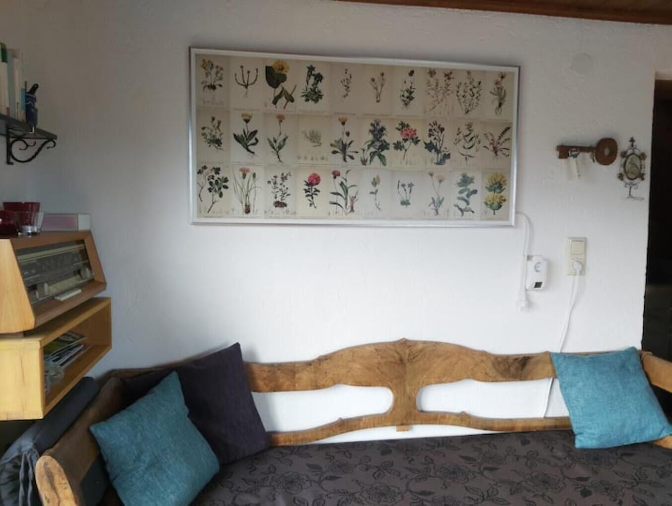 A room with a wooden headboard sofa, a wall-mounted botanical illustration, and a vintage key on the wall.