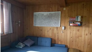 Et hyggeligt rum med en blå sofa, et lille bord, en træbænk, en vægmonteret reol med bøger og et stort abstrakt maleri.