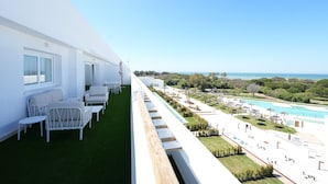 Un balcón con mobiliario blanco, una zona de piscina y vistas al océano.