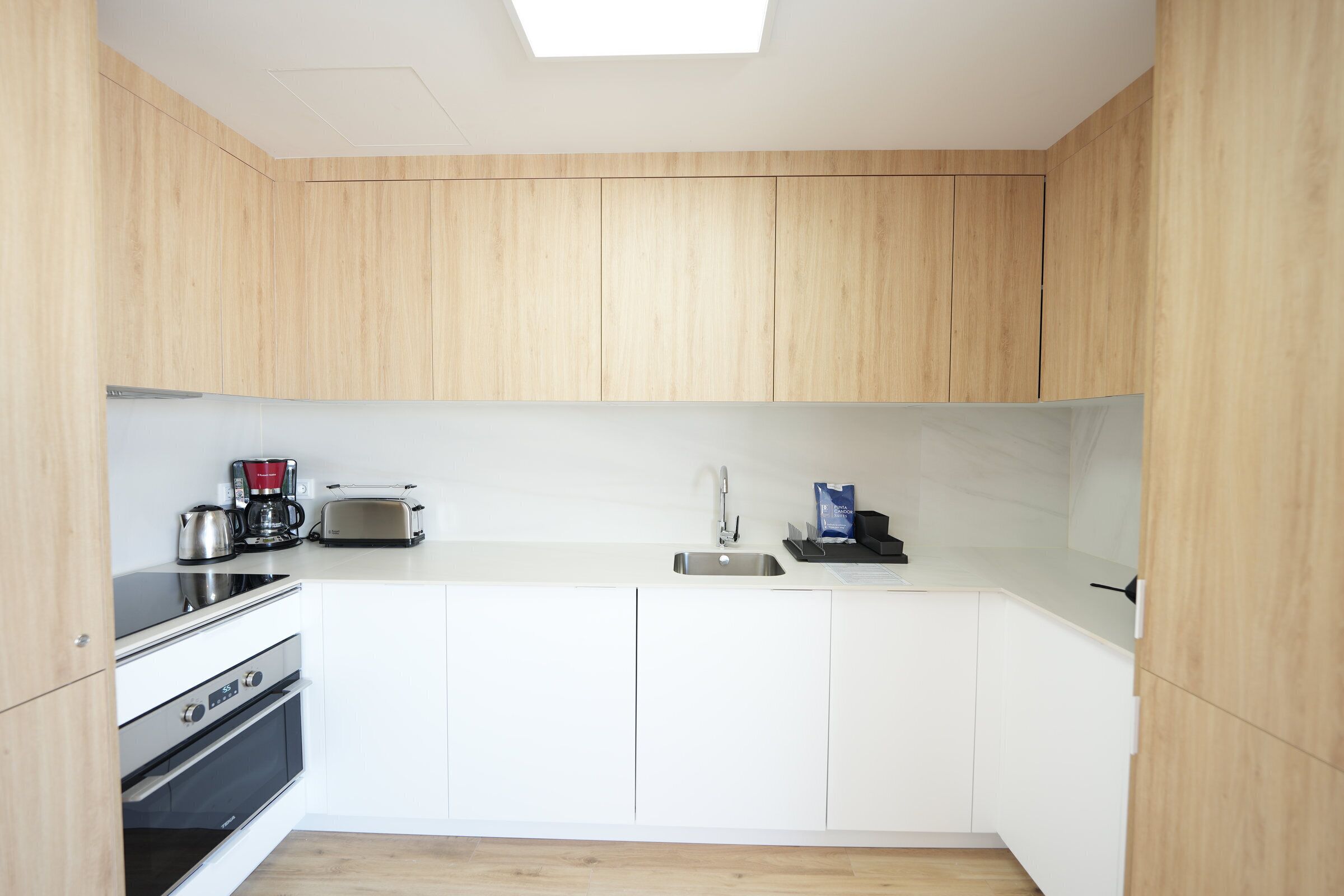 A modern kitchen with wooden cabinets, a built-in oven, a toaster, and a sink.