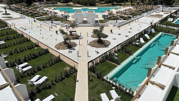 Un resort con una piscina amplia, numerosas tumbonas y un jardín central.