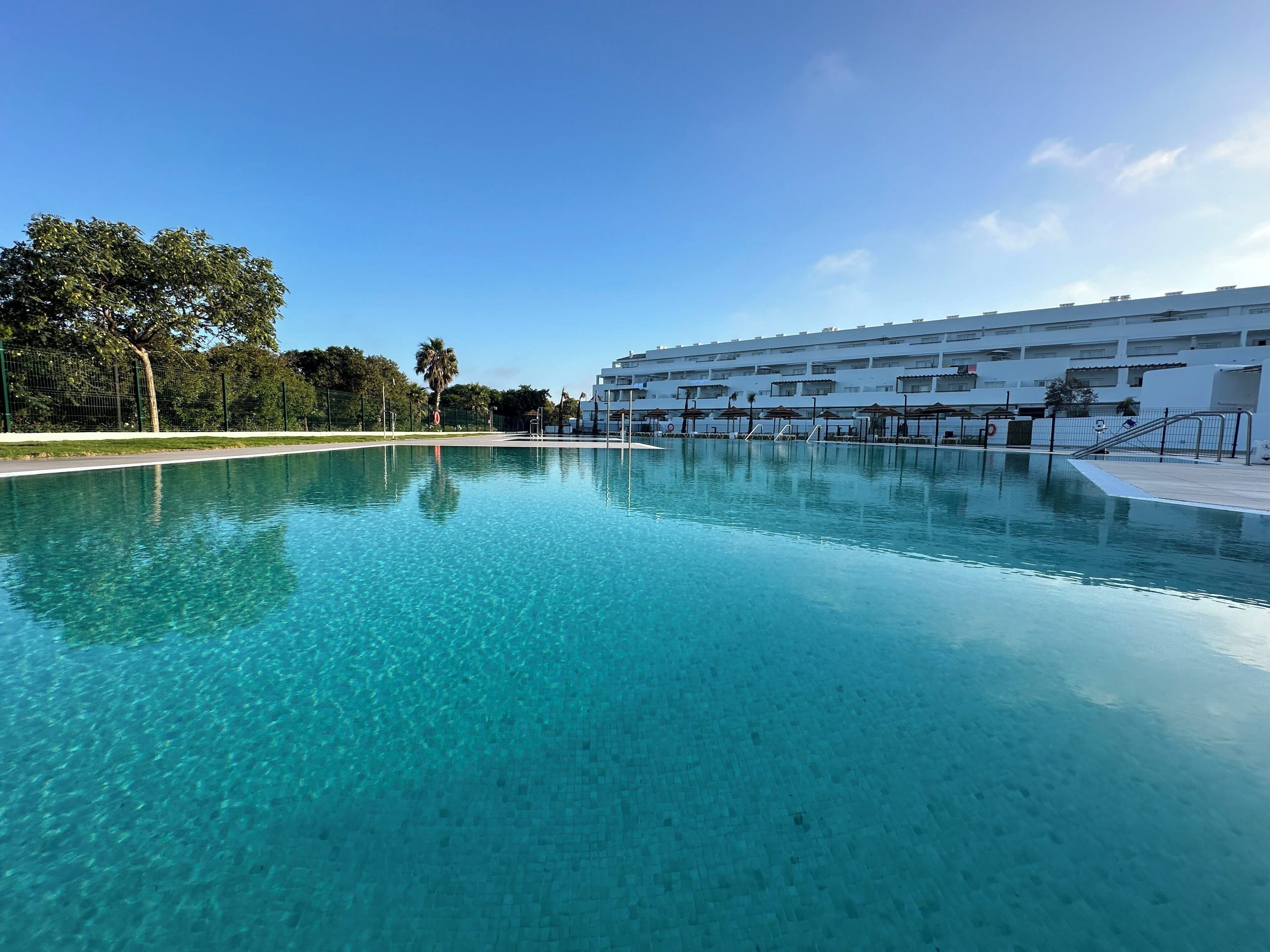 Una piscina azul cristalina con un edificio moderno al fondo.