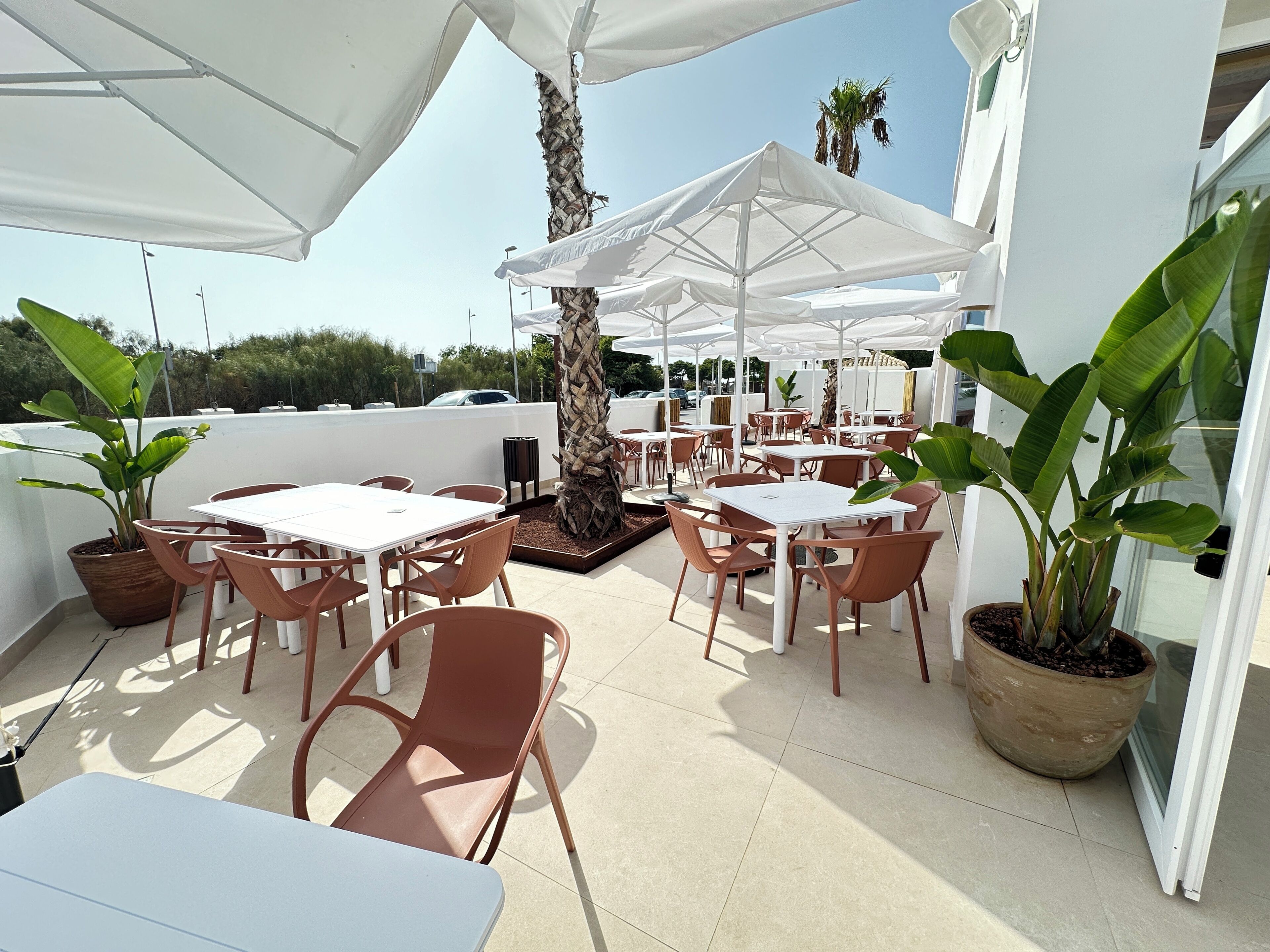 An outdoor patio area with white tables and chairs, umbrellas, and potted plants.