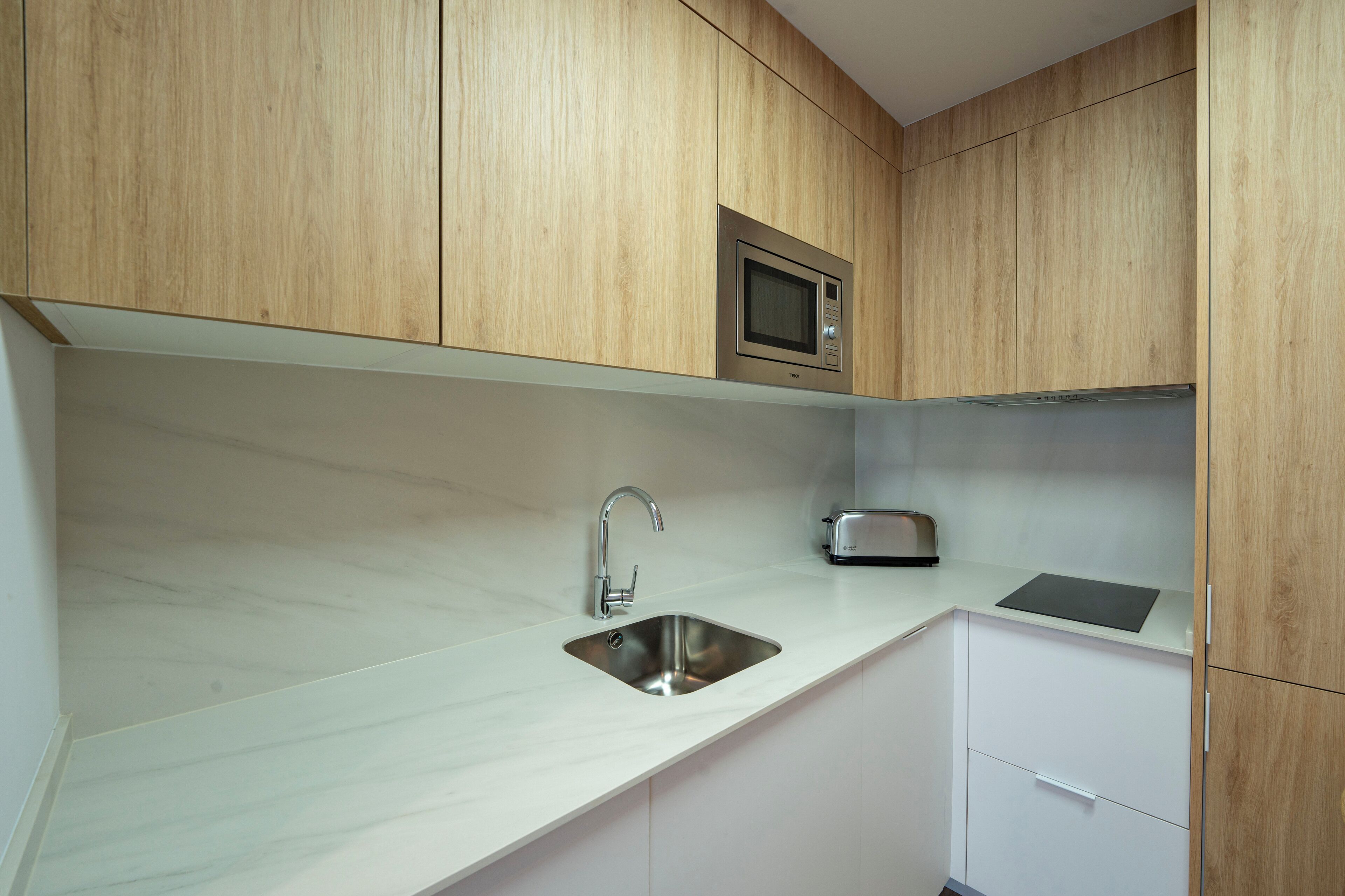 A kitchen with wooden cabinets, a stainless steel sink, a microwave, and a toaster.