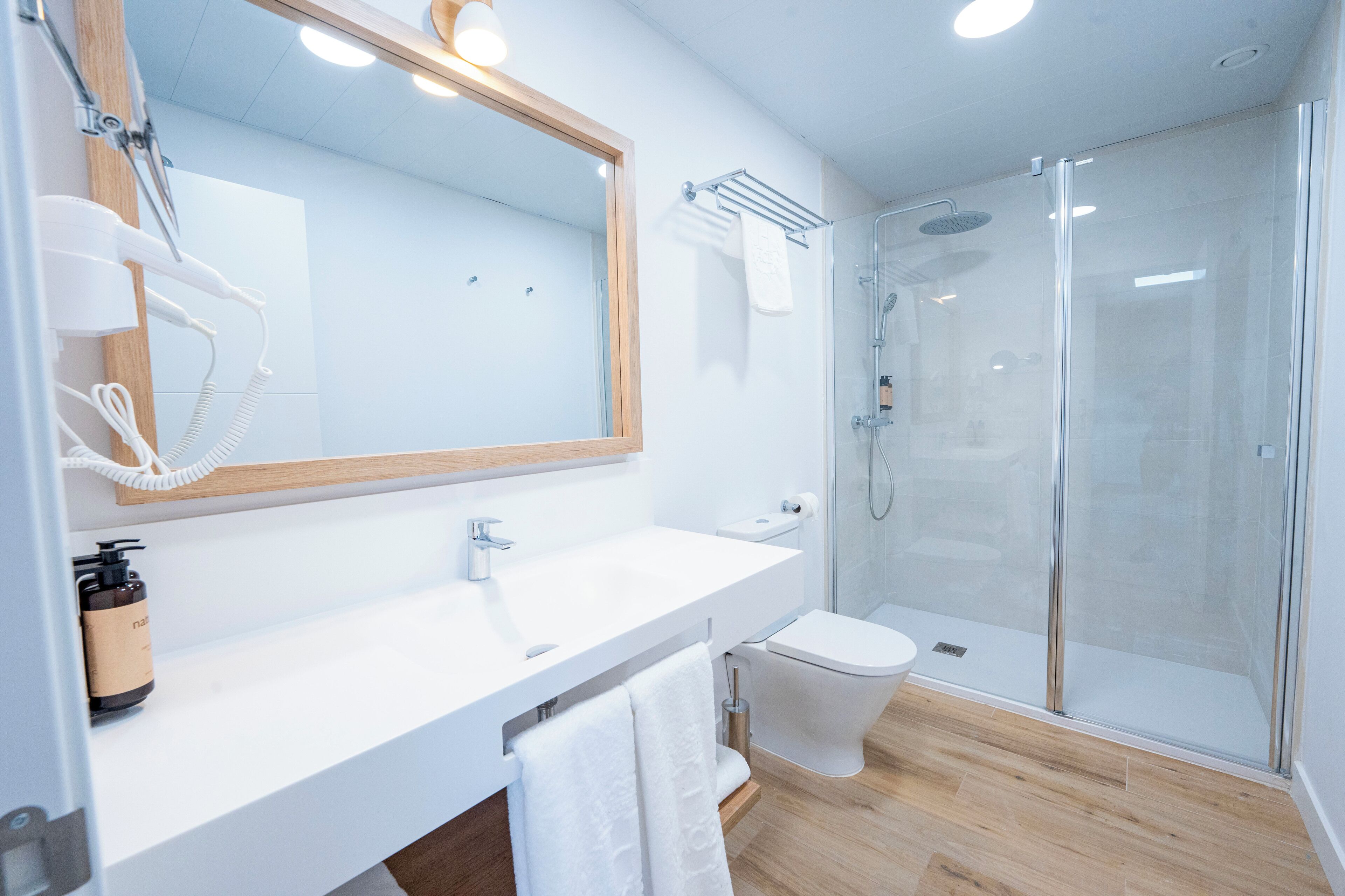 A modern bathroom with a white sink, a mirror, a glass shower enclosure, and a toilet.