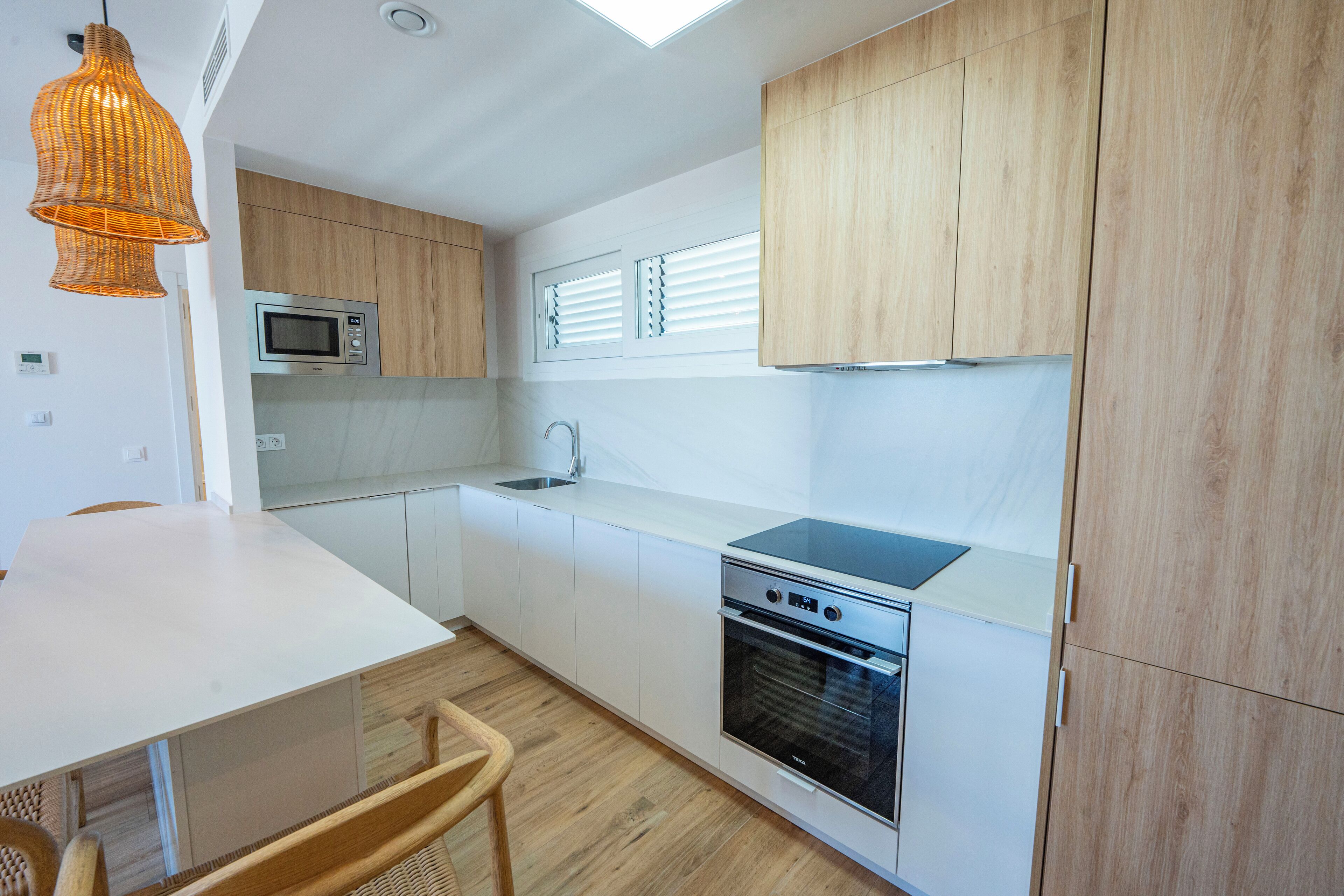 Una cocina moderna con armarios blancos, un microondas, una estufa y una lámpara colgante.