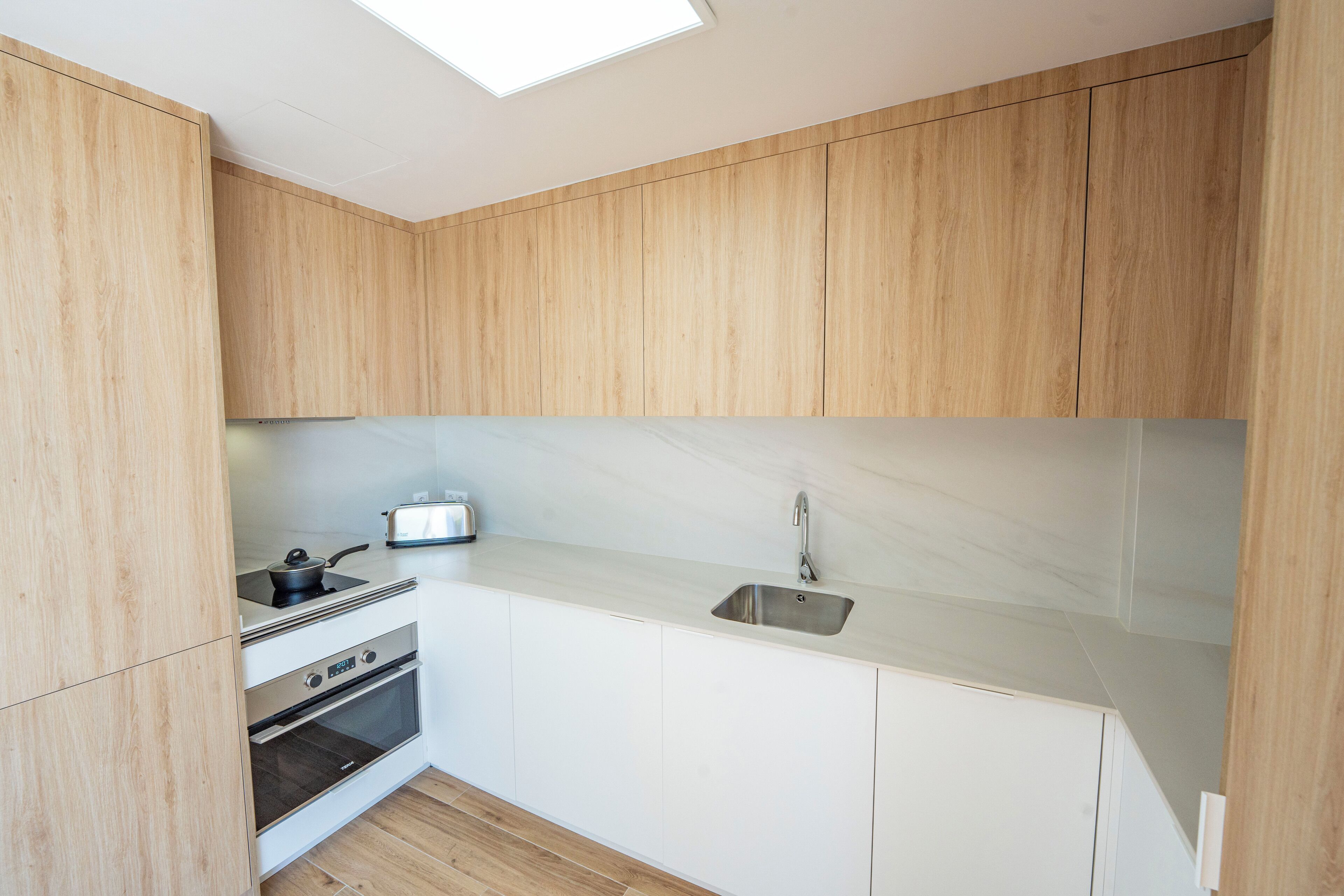 Eine moderne Küche mit Holzschränken, einer Edelstahlspüle, einem Einbauofen und einem Toaster.
