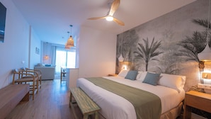 Un dormitorio con una cama grande, ventilador de techo, un mural en la pared y una zona de comedor con sillas y un banco.