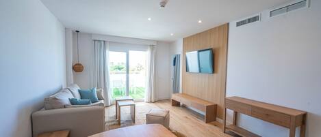 A modern, well-lit room with a wooden dining table, a sofa, a bench, and a TV mounted on the wall.
