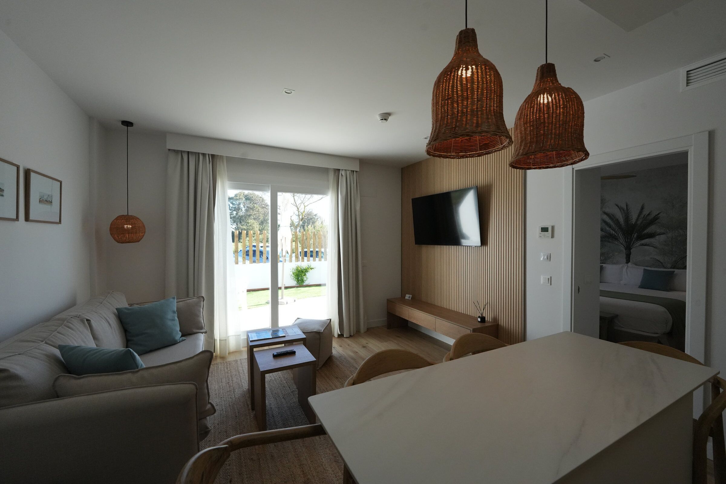 A modern living room with a sofa, a dining table, and a TV mounted on the wall.