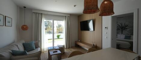 A modern living room with a sofa, a dining table, and a TV mounted on the wall.