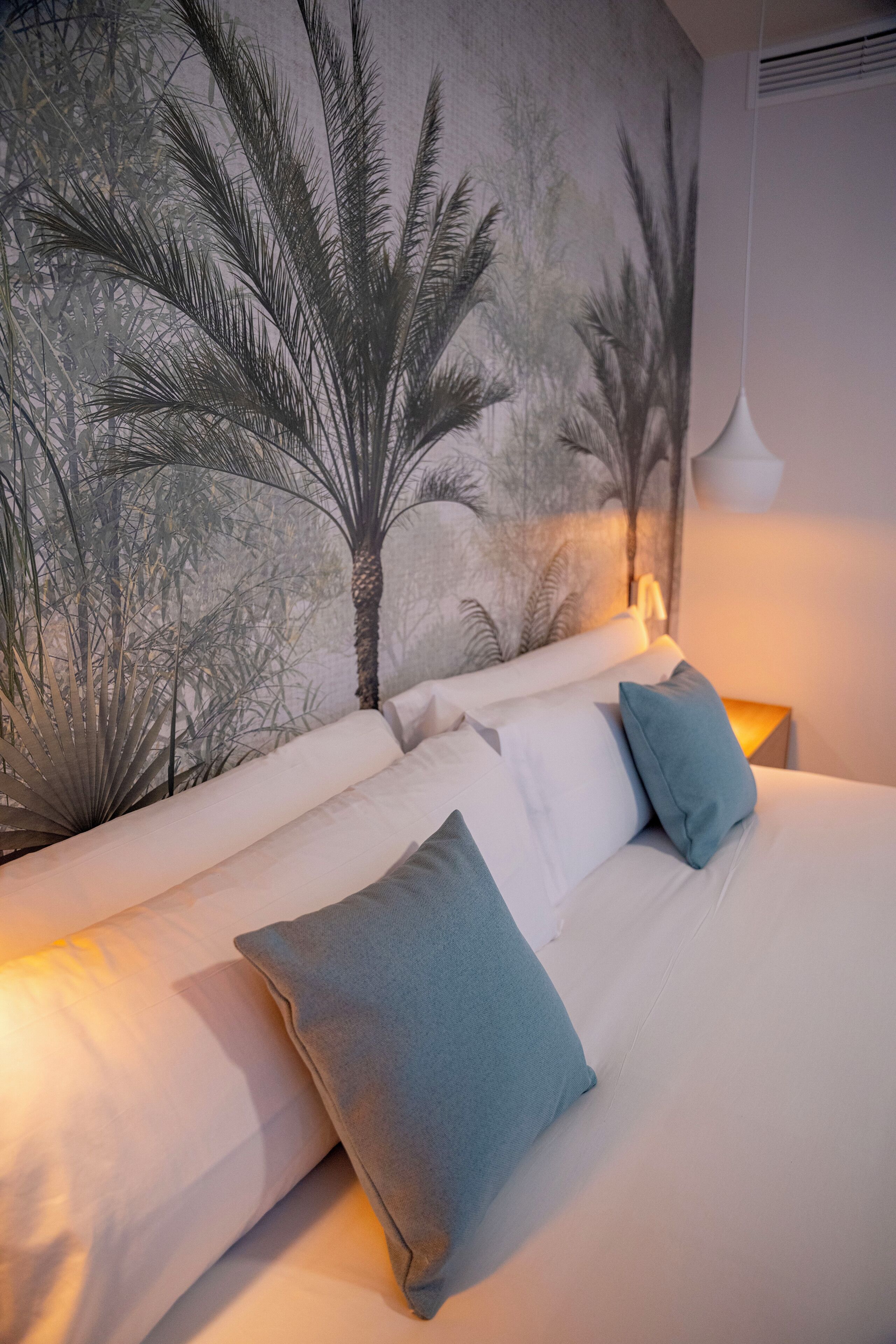 Une chambre avec un grand lit, du linge de lit blanc et une fresque représentant des palmiers sur le mur.