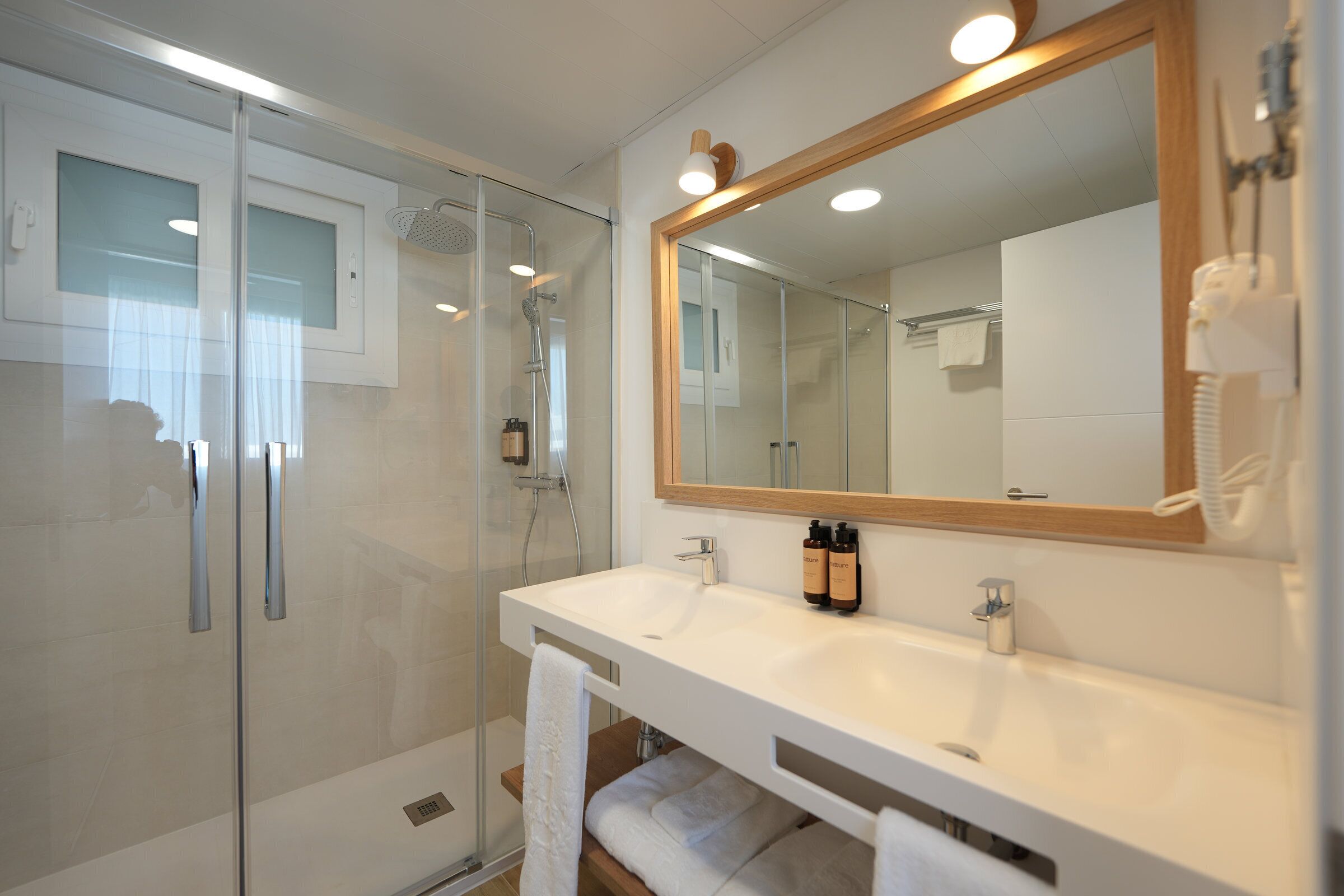 A modern bathroom with a glass shower enclosure, a white sink with a large mirror, and a towel rack.