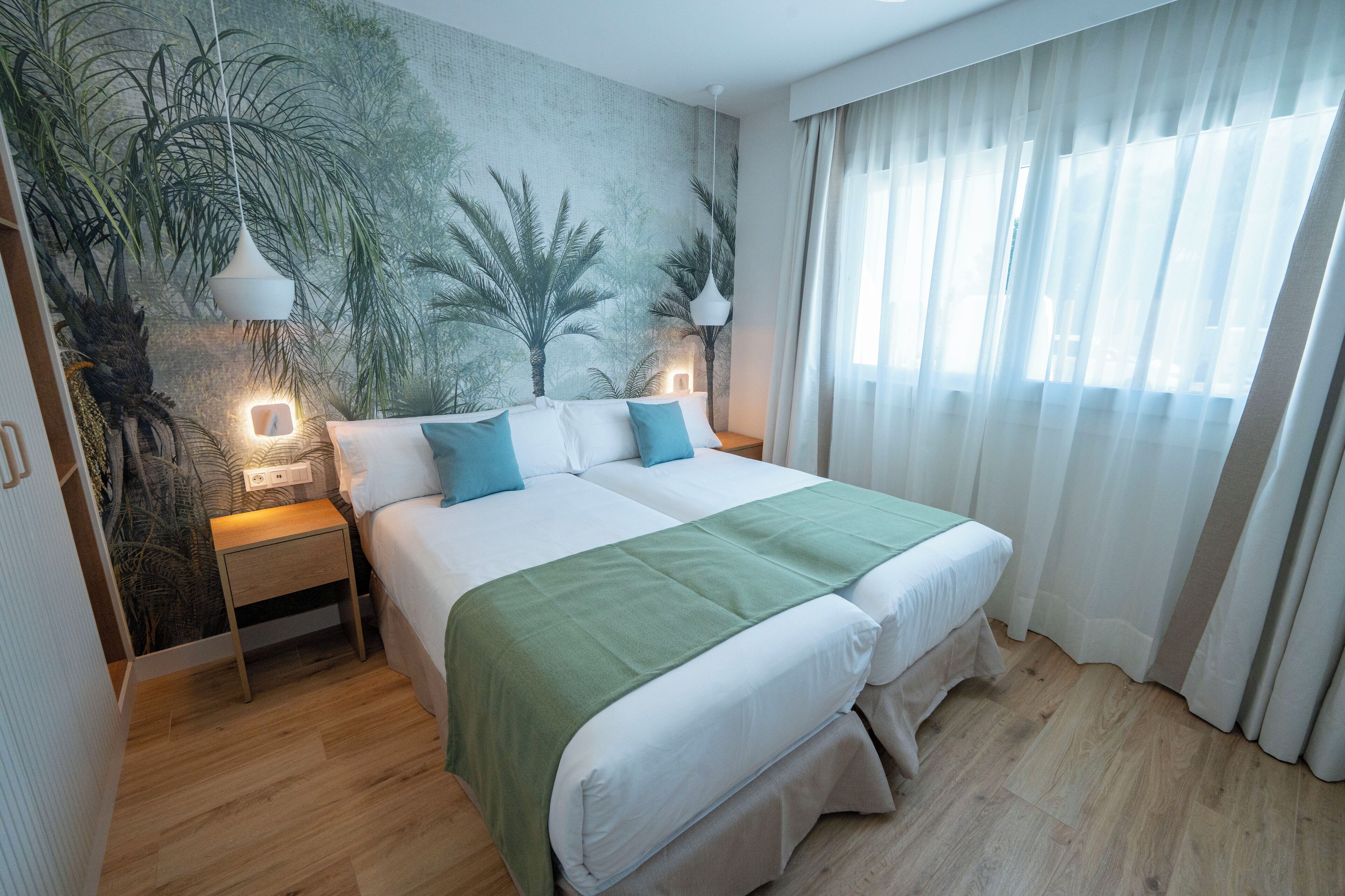 Ein ordentlich eingerichtetes Schlafzimmer mit einem großen Bett, einem Nachttisch, einer Wandmalerei und einem Fenster mit durchscheinenden Vorhängen.