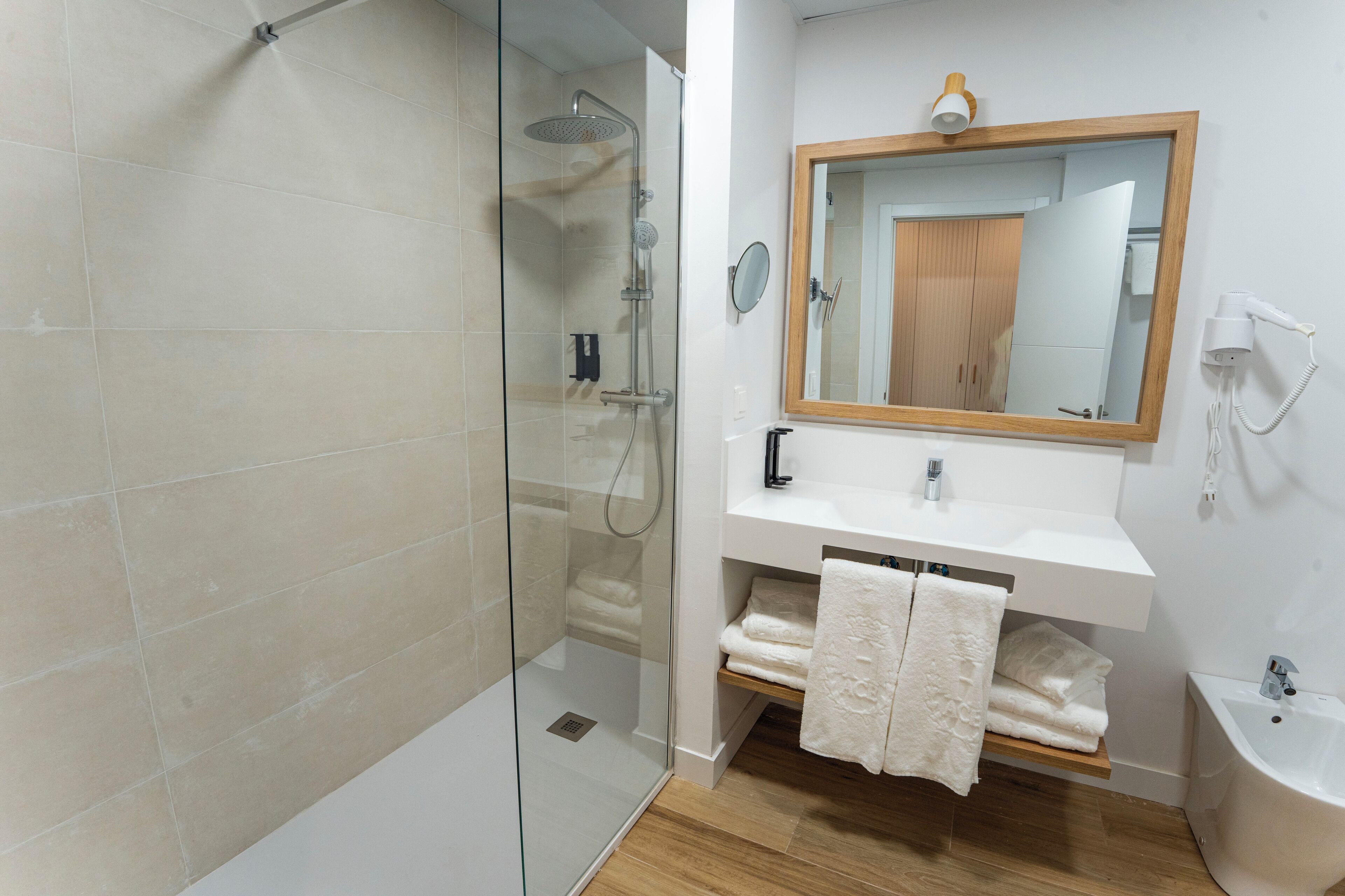 A modern bathroom with a glass-enclosed shower, a wooden vanity with a mirror, and a bidet.