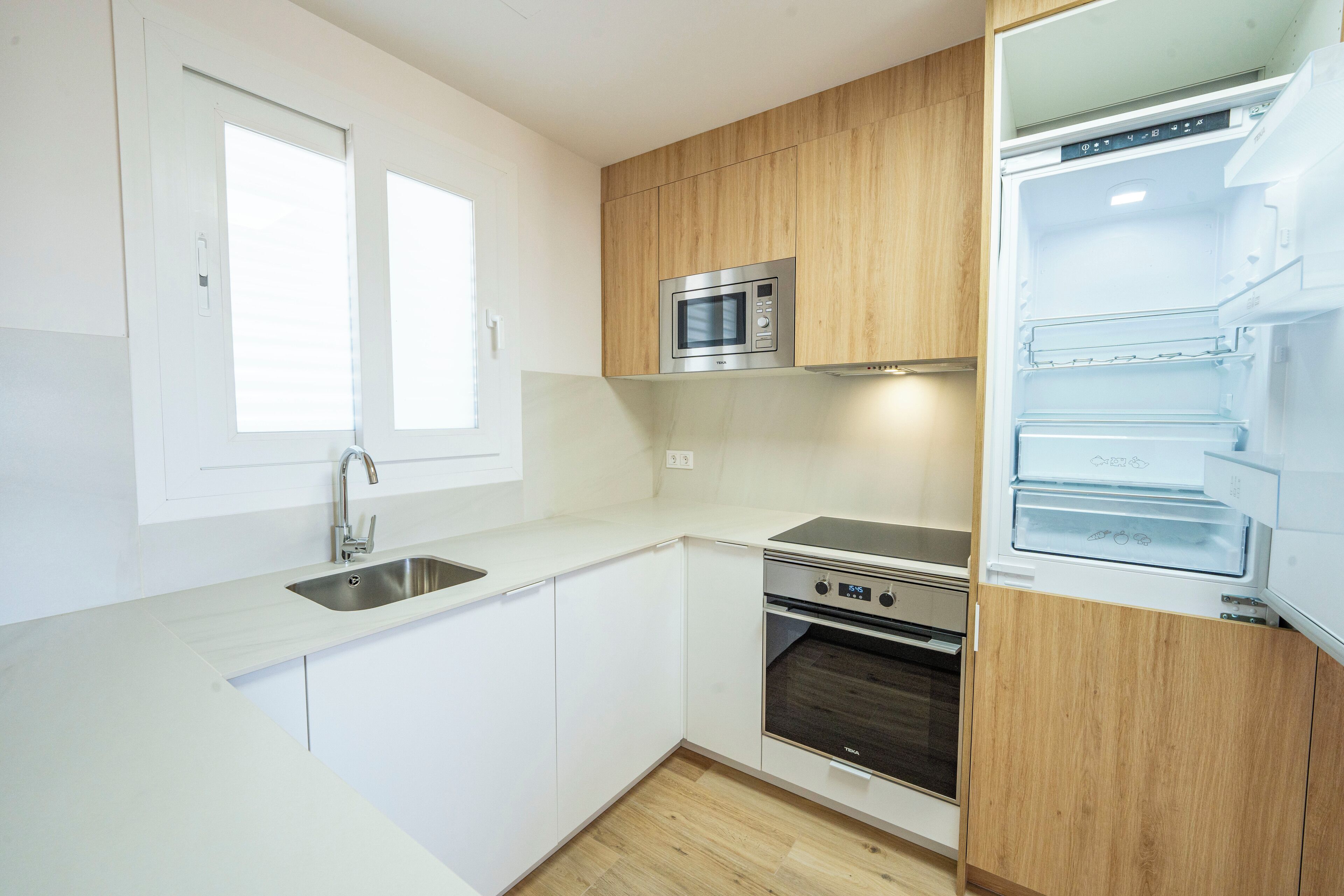Een moderne keuken met witte kastjes, een roestvrijstalen spoelbak, een magnetron, een oven en een geïntegreerde koelkast.