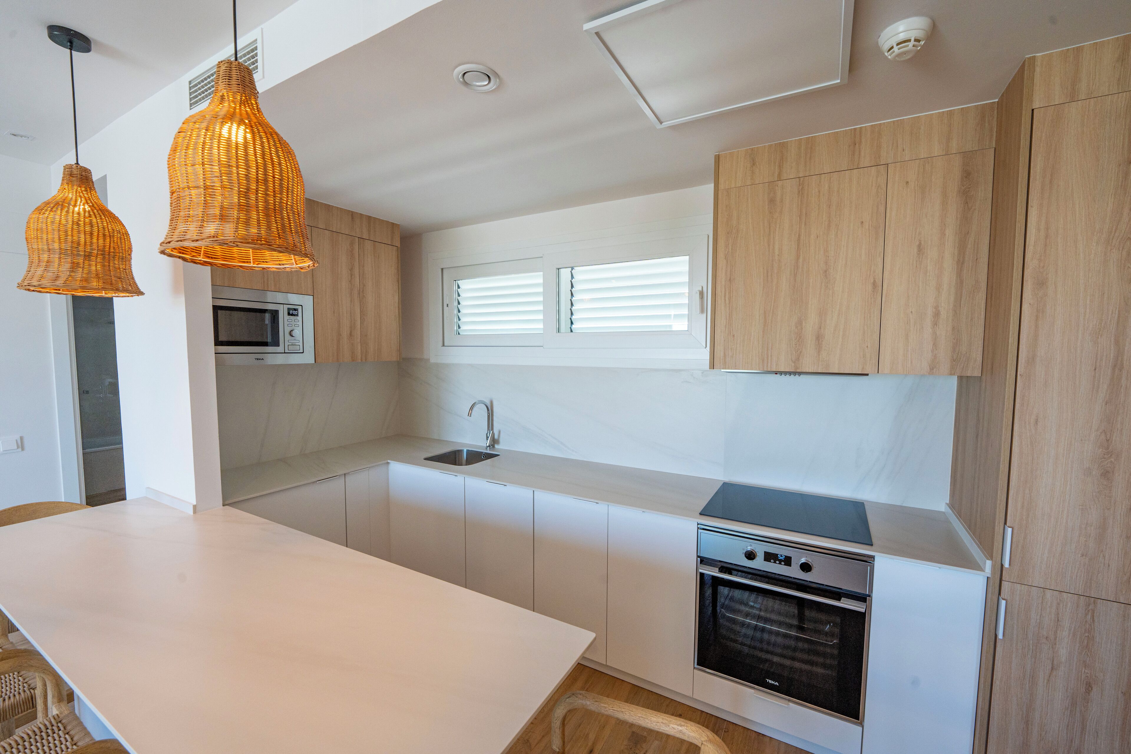 A modern kitchen with white cabinets, a built-in microwave, a stove, and two hanging wicker pendant lights.