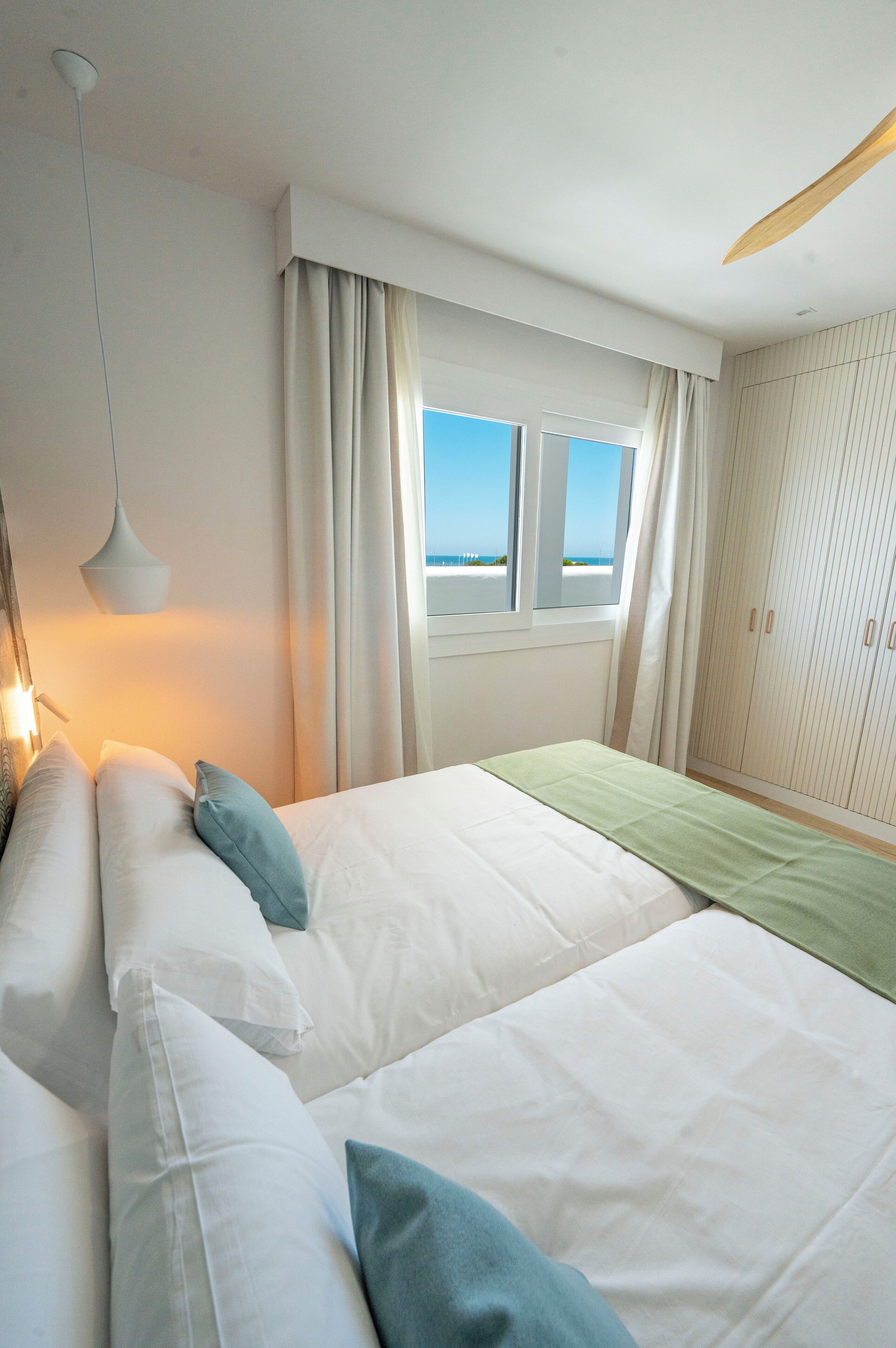 A hotel room with a bed, a window with curtains, a wardrobe, and a hanging light fixture.