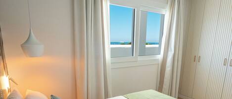 A hotel room with a bed, a window with curtains, a wardrobe, and a hanging light fixture.