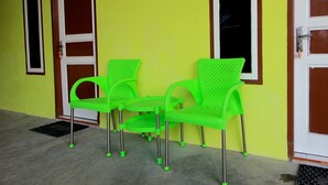 Un edificio con fachada amarilla brillante, una puerta con el número '1' y dos sillas de plástico verde con patas de metal.