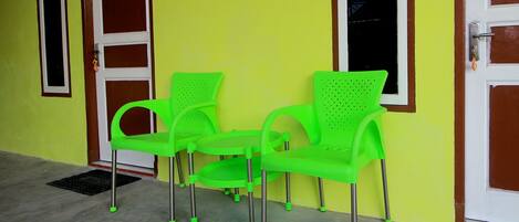 A building with a bright yellow exterior, a door with a number '1' sign, and two green plastic chairs with metal legs.