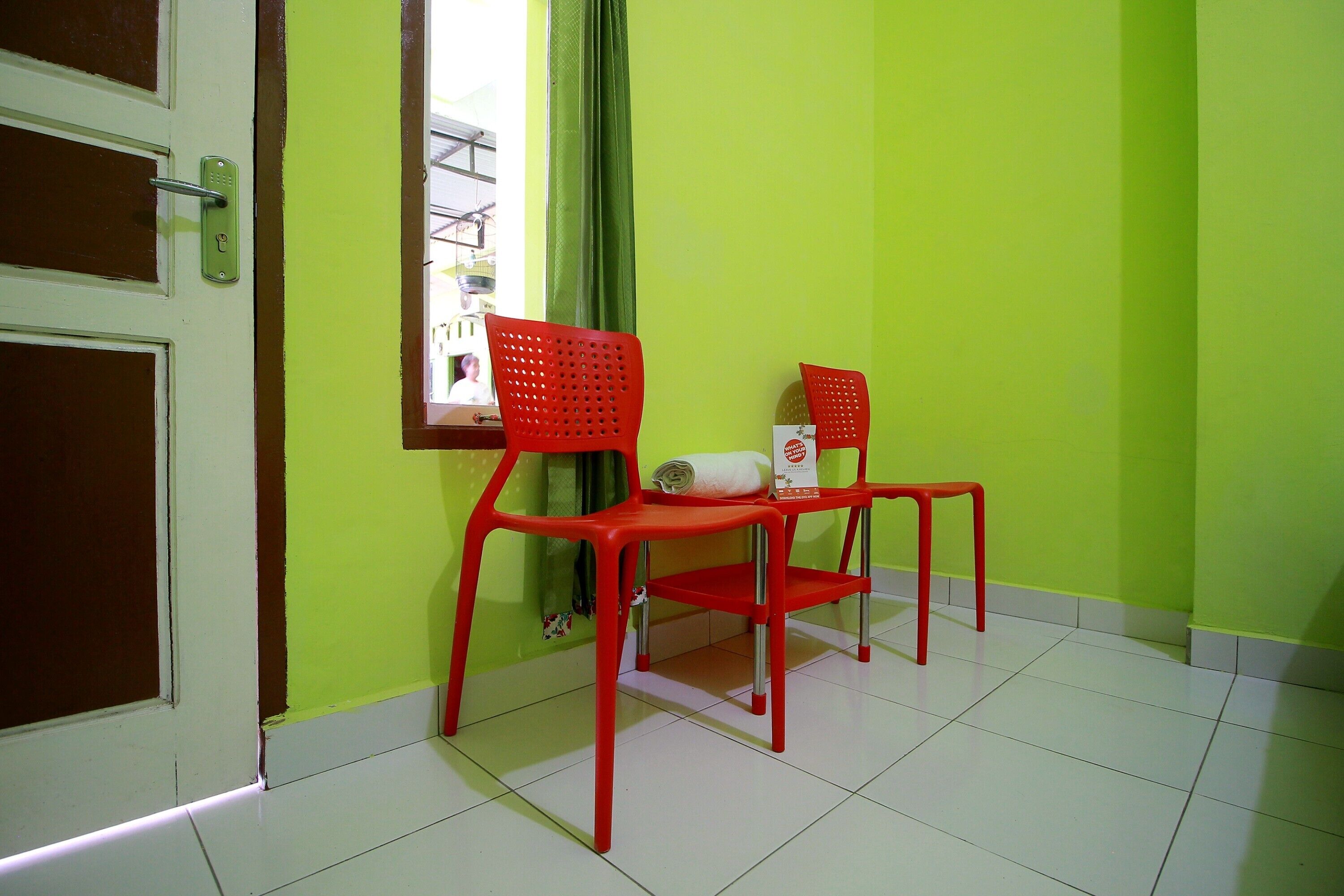 Una habitación con dos sillas rojas, una ventana con cortina y una puerta con picaporte.