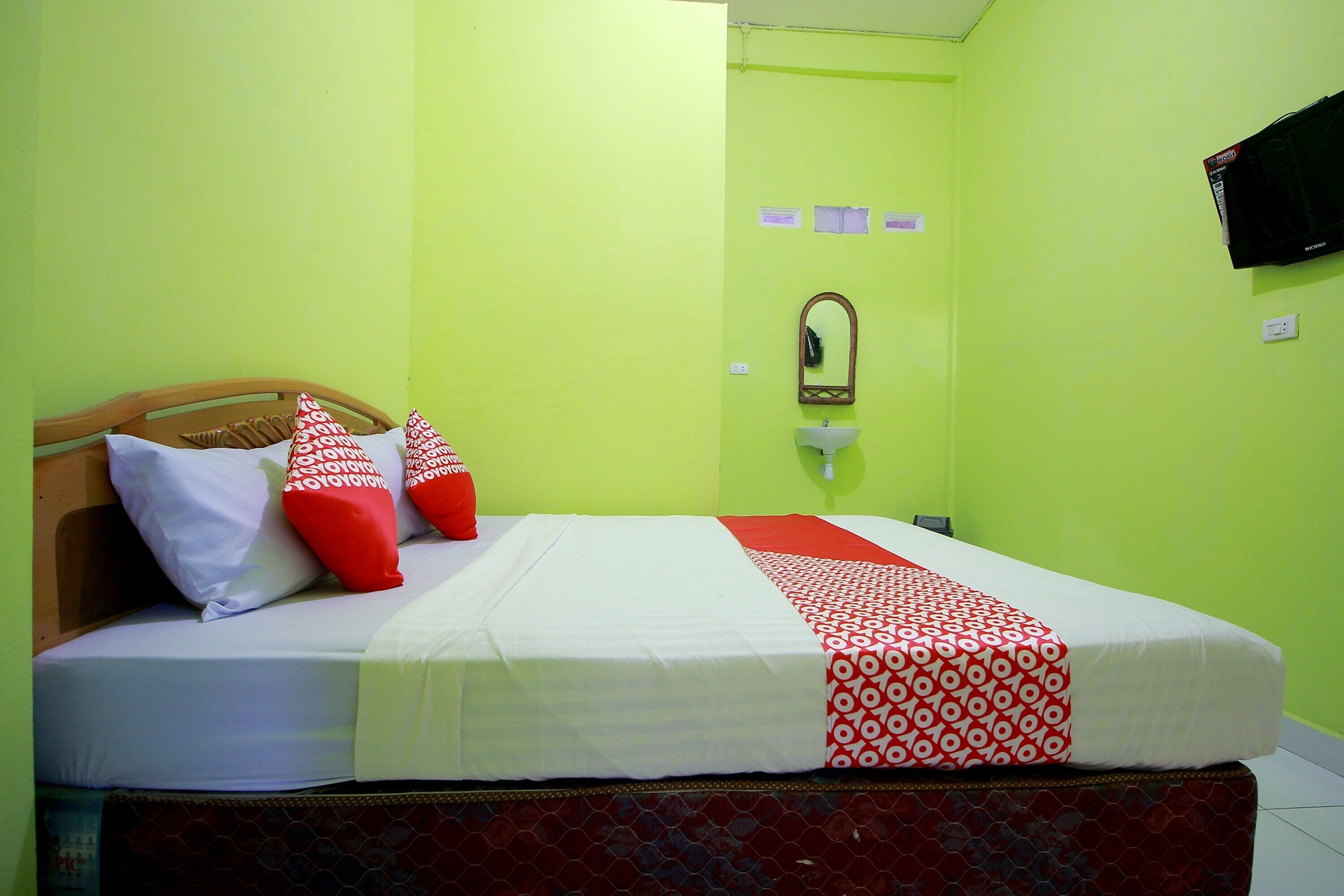 A hotel room with a bed, pillows, a mirror, and a television on the wall.