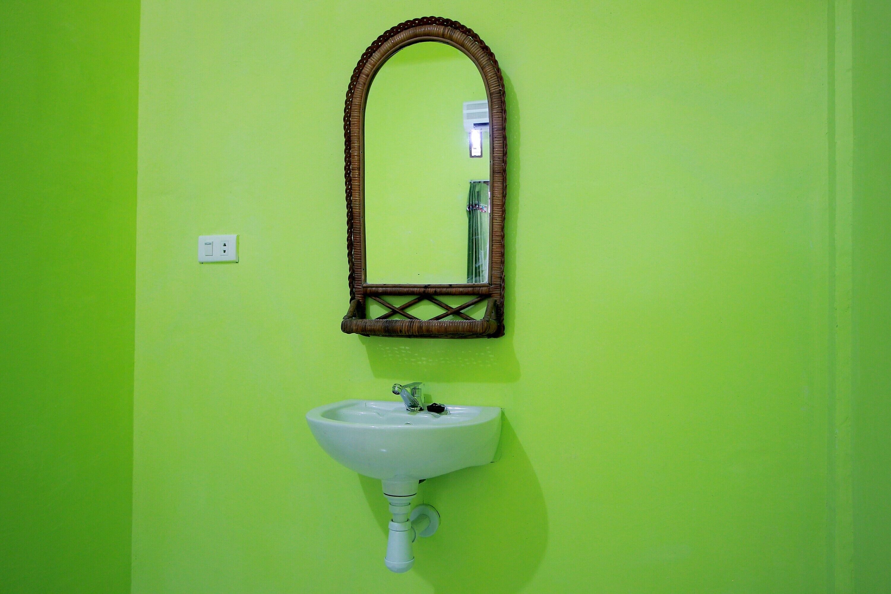 A bathroom with a green wall, a white sink, and a mirror with a wooden frame.