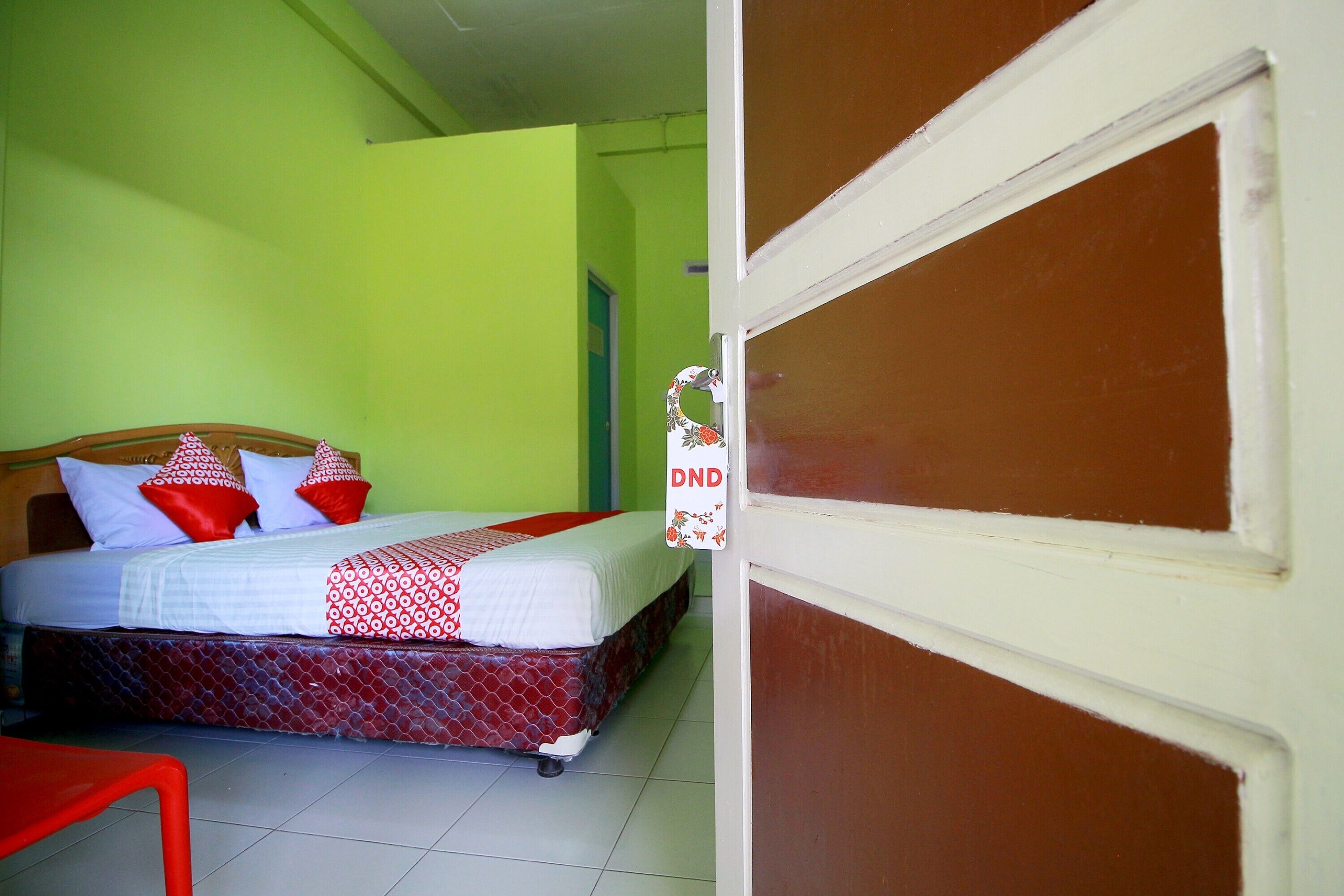 A hotel room with a bed, a red chair, and a door with a sign.