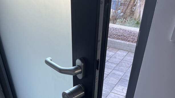 A modern door with a handle and lock, leading to an outdoor area with a tiled floor and a doormat. - Près Colmar 6 Dans Maison Moderne de 2023, à 10 mn de Colmar , 40 mn Europapark, (Wolfgantzen)