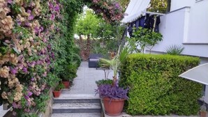 Ein schmaler Pfad führt zu einer Treppe, gesäumt von üppiger Vegetation und Topfpflanzen.