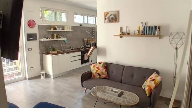 Ein modernes Wohnzimmer mit einer Couch, einem Couchtisch und einer Küche im Hintergrund.