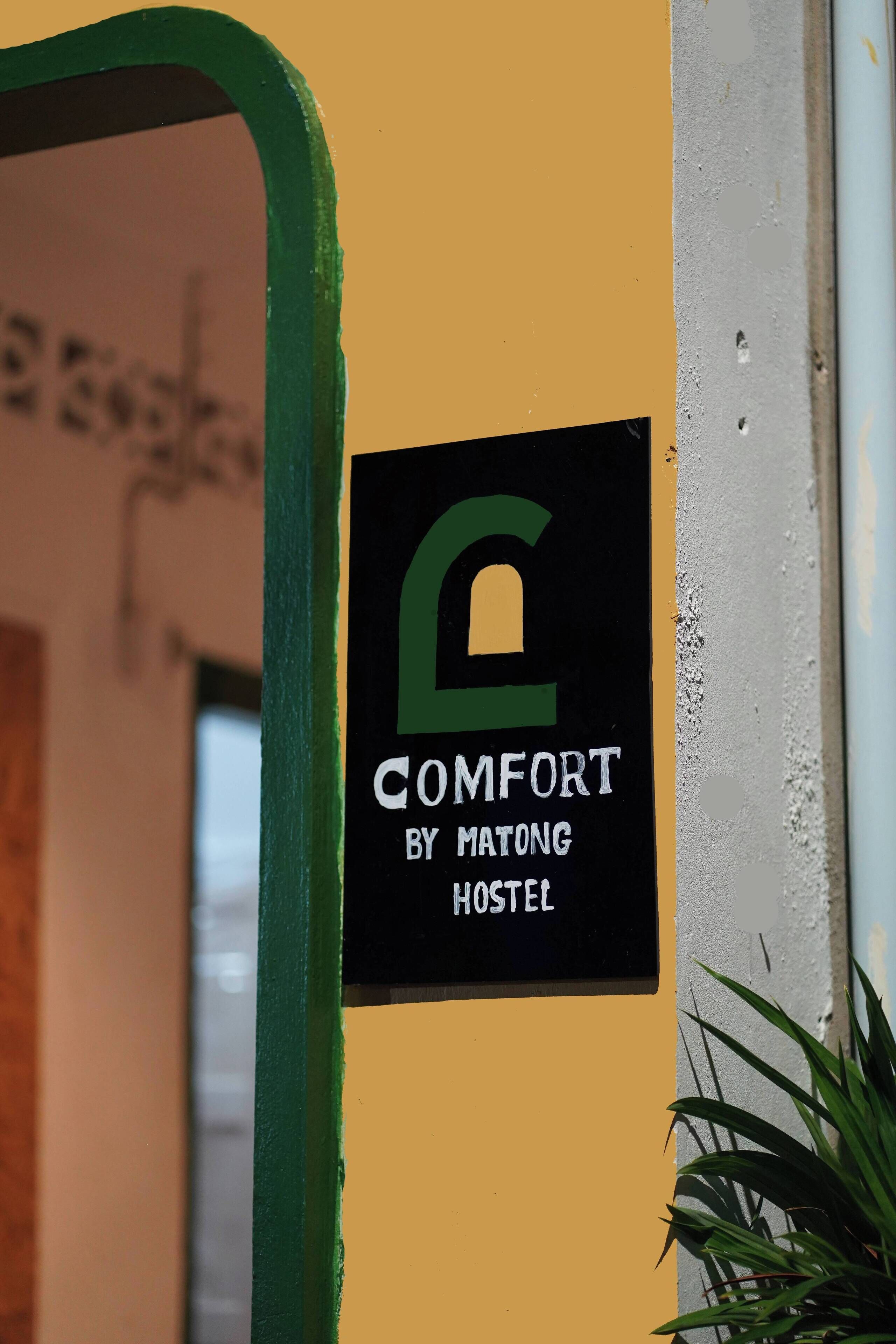 A hostel sign with a green frame and a black background, featuring a lock symbol and the text "COMFORT BY MATONG HOSTEL".