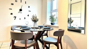 A dining area with a round table set for four, a wall clock, and a window with plants. - Spacious House |  Parking | Long Stay Discount (Hamilton)