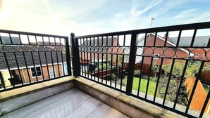A balcony with a black metal railing, a concrete floor, and a view of a residential area with houses and a lawn. - Spacious House |  Parking | Long Stay Discount (Hamilton)