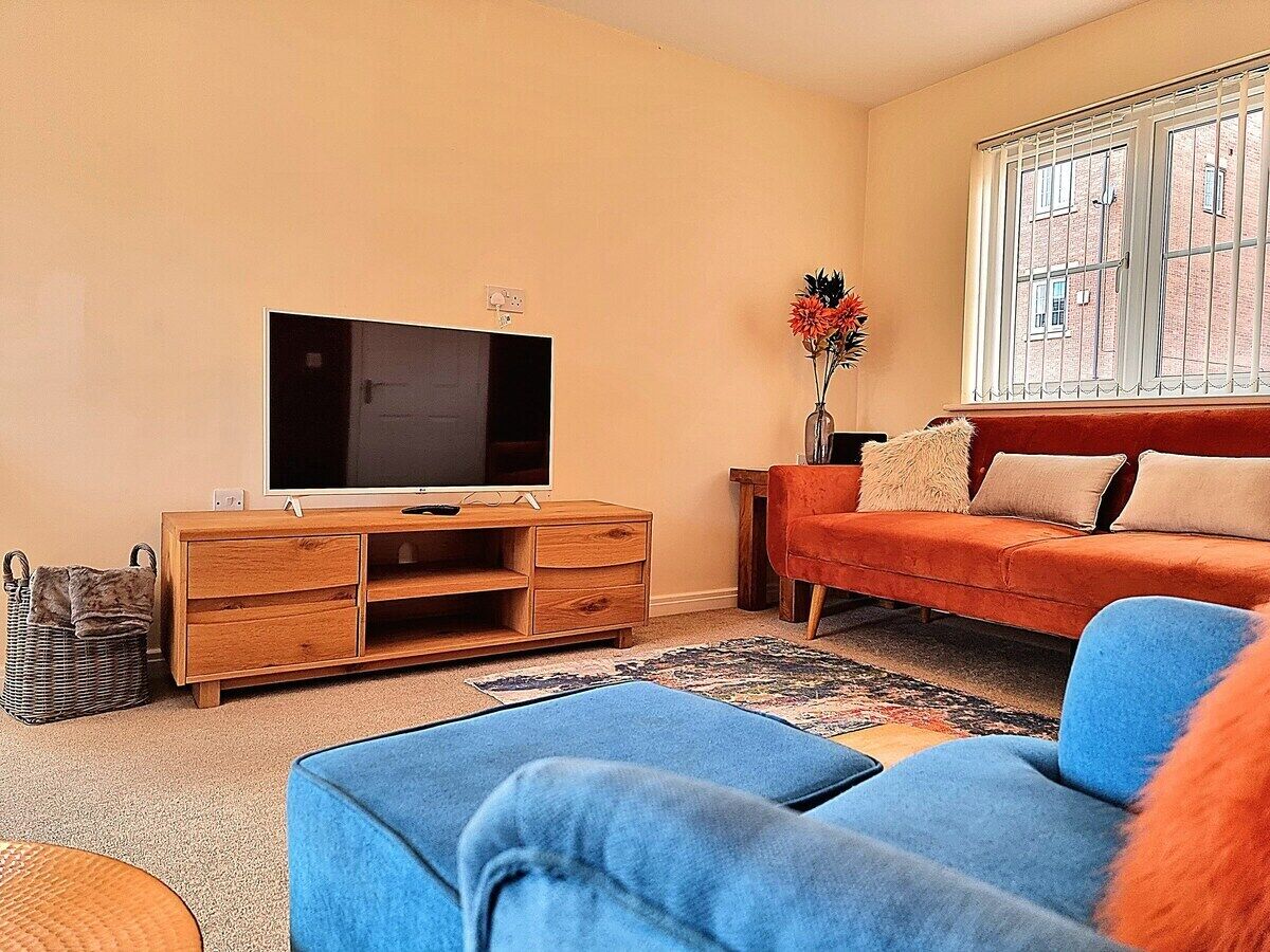 Een woonkamer met een flatscreen televisie op een houten kast, een blauwe bank, een rode bank, en een raam met tralies.