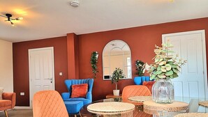 A living room with a glass coffee table, orange and blue chairs, and a vase with flowers. - Detached House w/Free Parking | Long Stay Discount (Leicestershire)