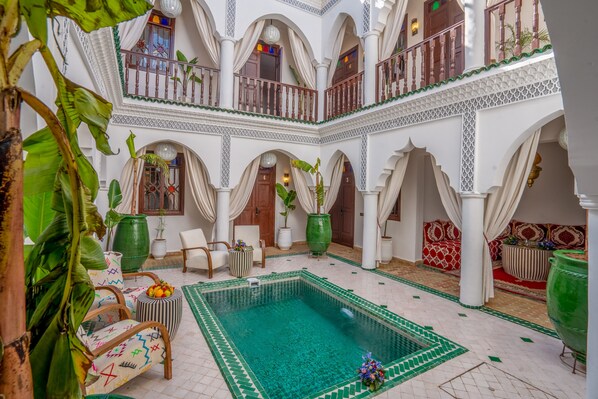 Un amplio patio con piscina central, varias zonas de estar y detalles arquitectónicos ornamentales.