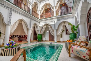 Un área de piscina interior lujosa con una piscina central, múltiples zonas de estar y detalles arquitectónicos ornamentales.
