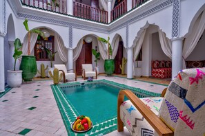 Un área de piscina con suelo de baldosas, una piscina y plantas en macetas.