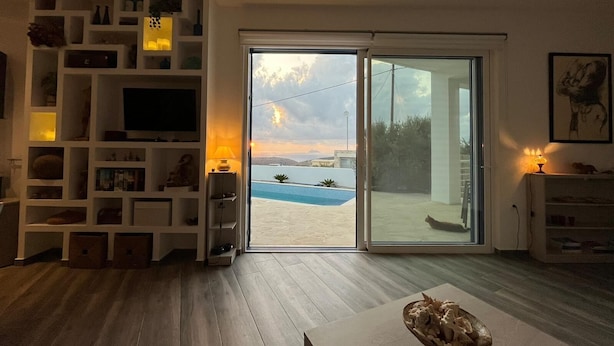 Ein modernes Wohnzimmer mit großem Fernseher, integrierten Regalen und Blick auf einen Pool und Berge.