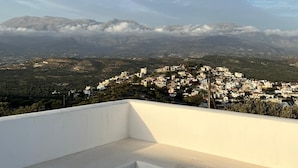 Eine Terrasse mit Tisch für zwei Personen, mit Blick auf eine Berglandschaft und ein Dorf weiter unten.