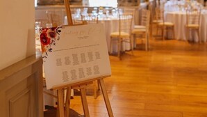 An indoor venue with wooden flooring, tables set for dining, and a menu stand with floral decorations.